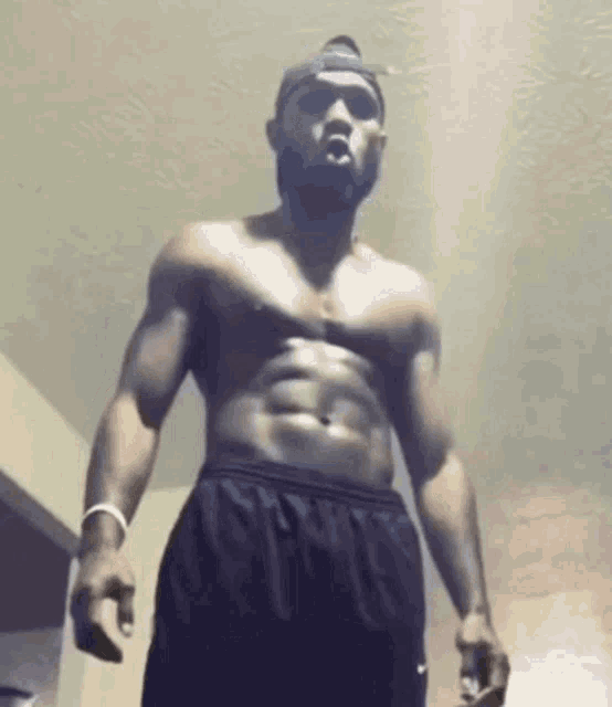a shirtless man with a beard is standing in a room with his mouth open .