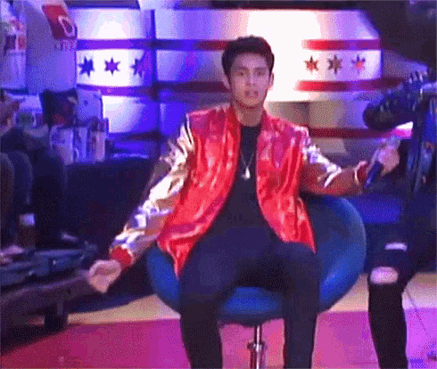 a man in a red jacket is sitting in a chair with his arms outstretched .