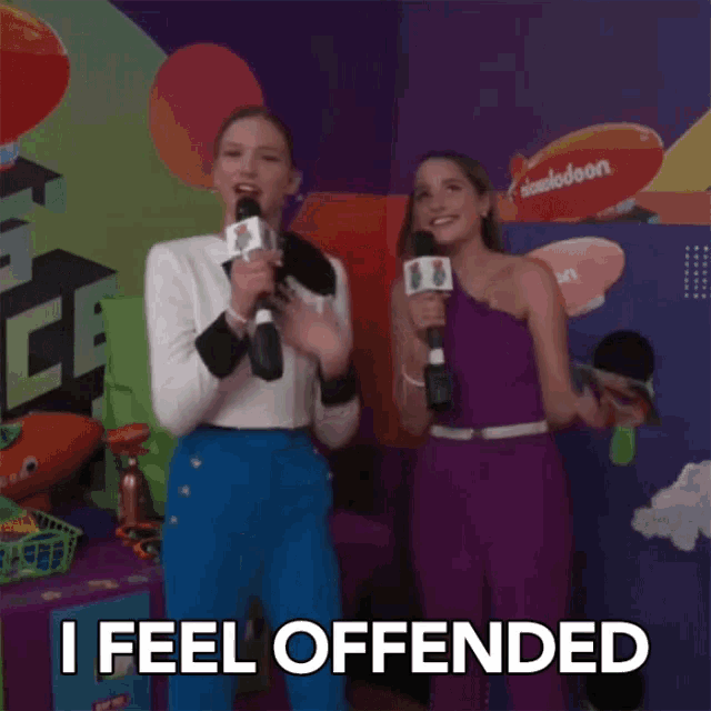 two women holding microphones in front of a nickelodeon sign saying " i feel offended "