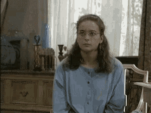a woman in a blue shirt and glasses is sitting in a chair in front of a window .