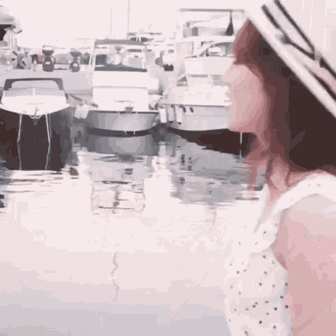 a woman in a hat is standing in front of boats in a harbor