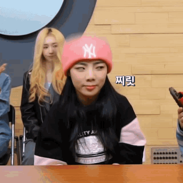 a woman wearing a pink ny hat is sitting at a desk