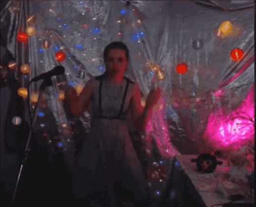 a woman singing into a microphone in front of a wall with balloons and lights