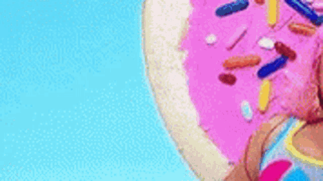a close up of a pink donut with sprinkles on it against a blue sky .