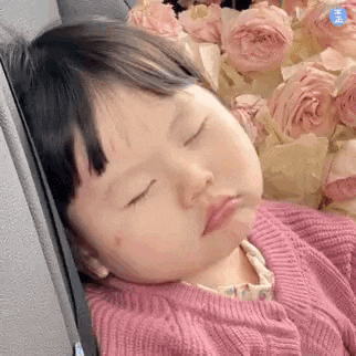 a little girl in a pink sweater is sleeping in a car seat next to a bouquet of pink roses .