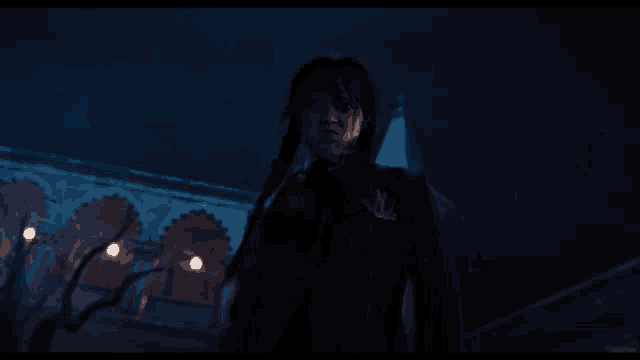 a woman with braids stands in front of a building with arches at night