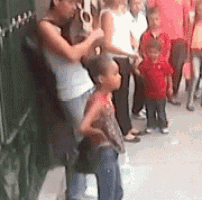 a group of people standing on a sidewalk including a woman holding a child