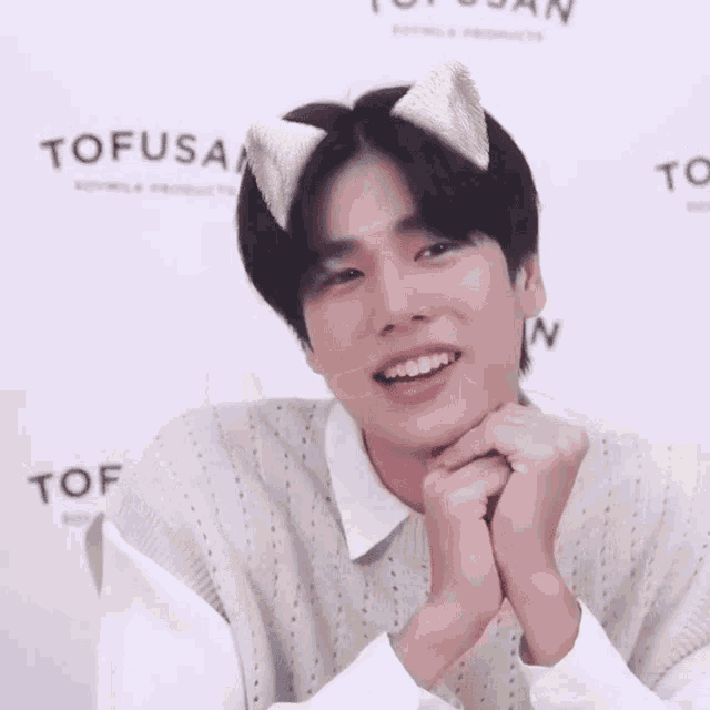 a young man wearing cat ears and a white shirt is smiling