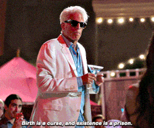 a man in a white suit and sunglasses holds a martini and says birth is a curse
