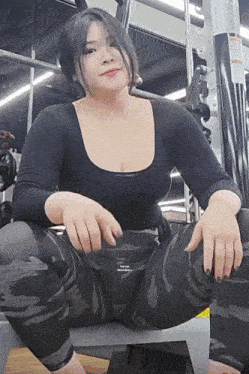 a woman is sitting on a bench in a gym wearing leggings and a black top .