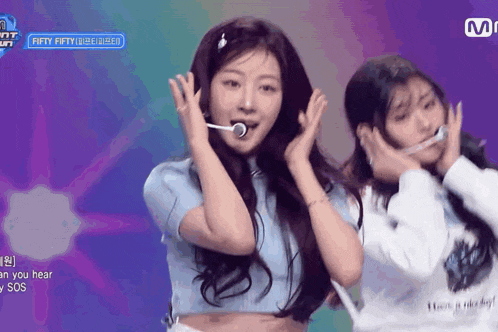 two girls are dancing on a stage with a sign that says fifty fifty in the background