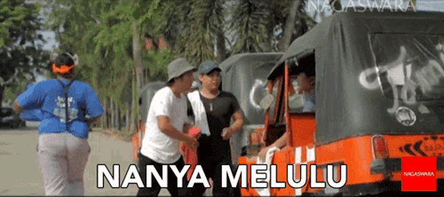 a group of people standing in front of an orange vehicle that says nanya melulu on it