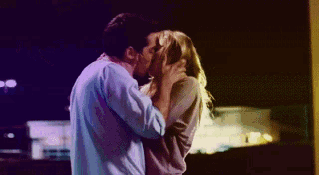 a man and a woman are kissing in front of a building at night