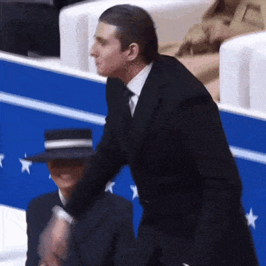 a man in a suit and tie stands next to a woman in a hat