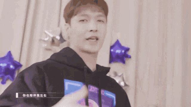 a young man in a black hoodie is dancing in front of a curtain .