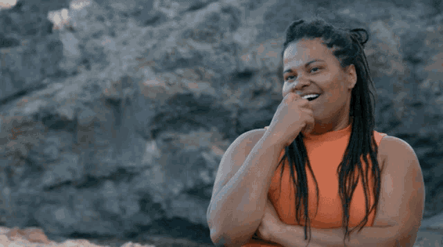a woman with dreadlocks wearing an orange tank top smiles