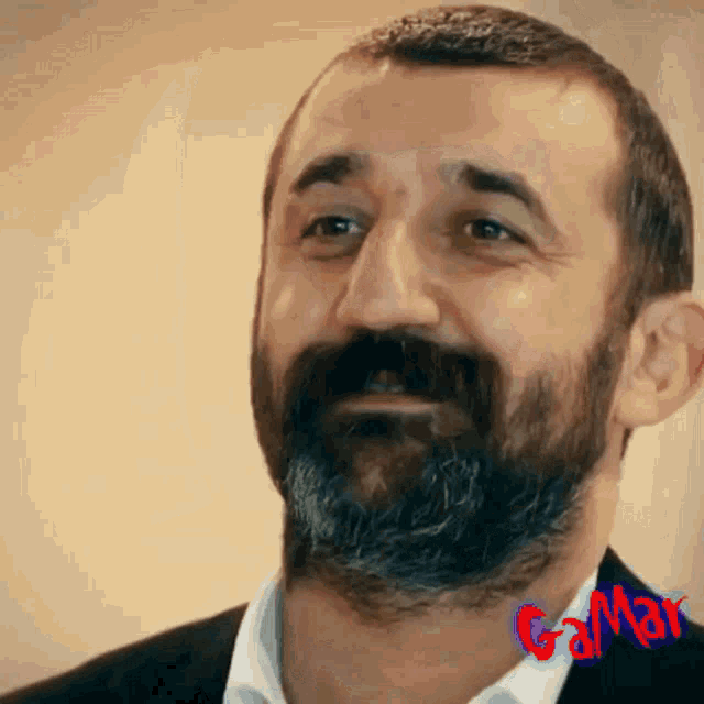 a man with a beard is smiling and the word gamar is on the bottom right