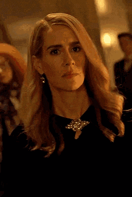a woman with blonde hair is wearing a black dress and earrings and looking at the camera .