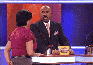 a man in a suit and tie is talking to a woman in a red shirt on a game show