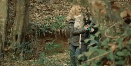 a man and a woman are standing in the woods looking at something .