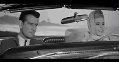 a man and a woman are sitting in a car looking at the rear view mirror .