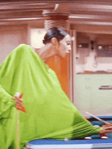 a person in a green blanket is standing in front of a pool table