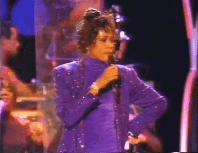 a woman in a purple dress is singing into a microphone on a stage