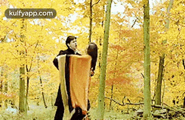 a man is holding a woman in his arms while standing in the woods .