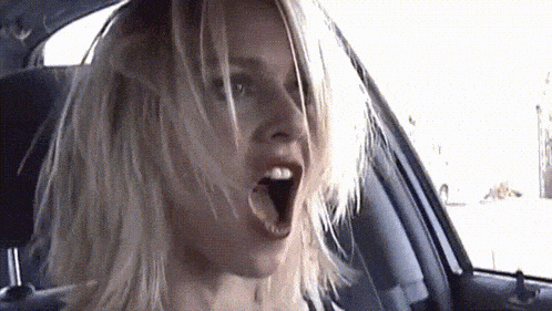 a woman with blonde hair is sitting in a car with her mouth wide open