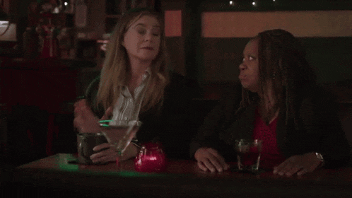 two women are sitting at a table drinking a martini .
