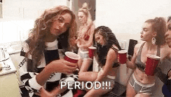 a group of women are sitting on the floor holding red cups and drinking beer .