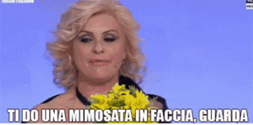 a woman is holding a bouquet of yellow flowers and says ti do una mimosata in faccia guarda .