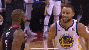 a basketball player wearing a golden state warriors jersey stands next to another player .