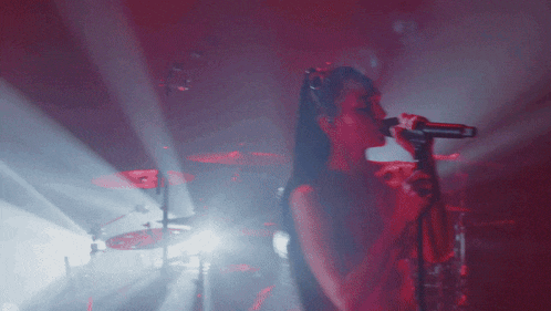 a woman singing into a microphone in a dark room with red lights