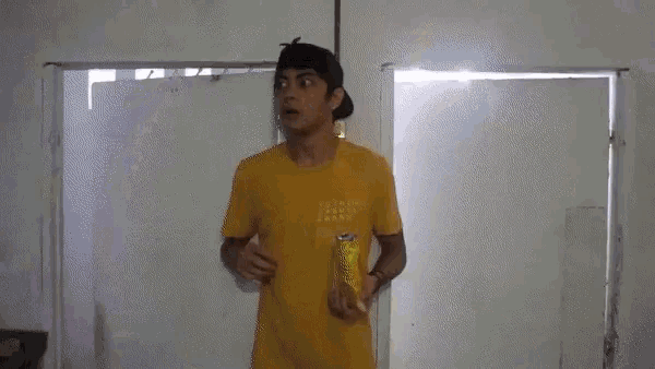 a man in a yellow shirt is making a surprised face while standing in front of a window .