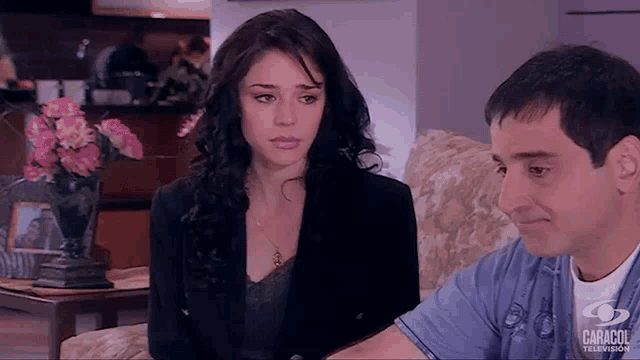 a man and a woman are sitting on a couch and the man is wearing a blue shirt with caracol television written on it