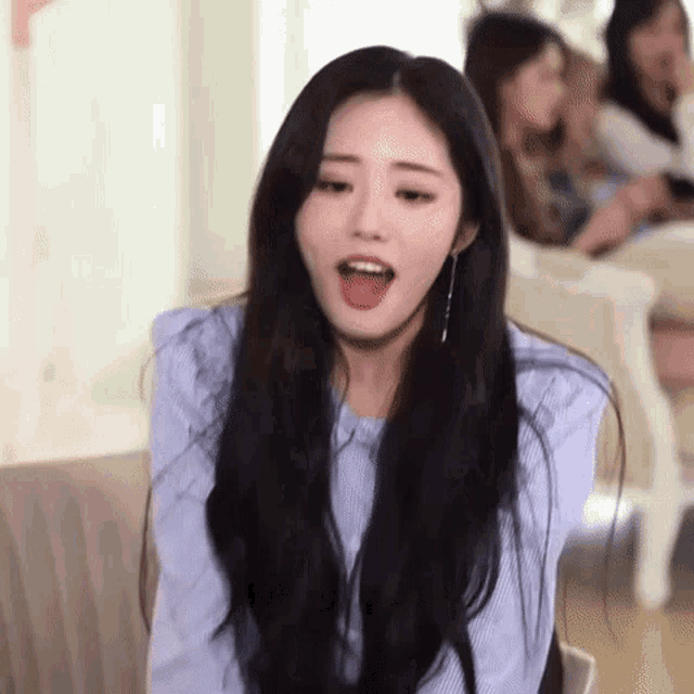 a woman with long black hair is sitting in a chair with her mouth open and making a funny face .
