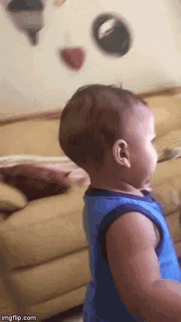 a baby in a blue tank top is standing in front of a couch