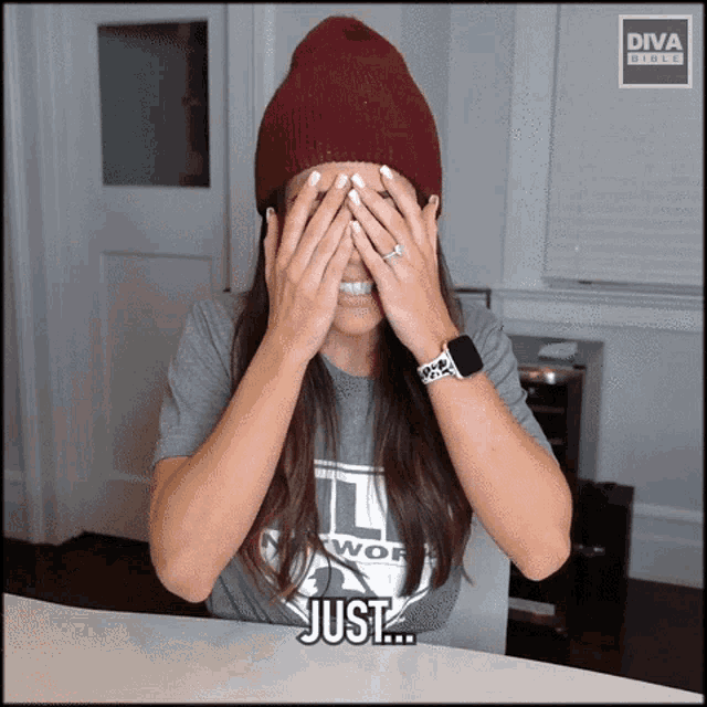 a woman wearing a beanie and a diva shirt covering her eyes with her hands