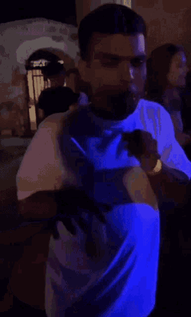 a man in a white shirt is dancing in a dark room with a blue light behind him