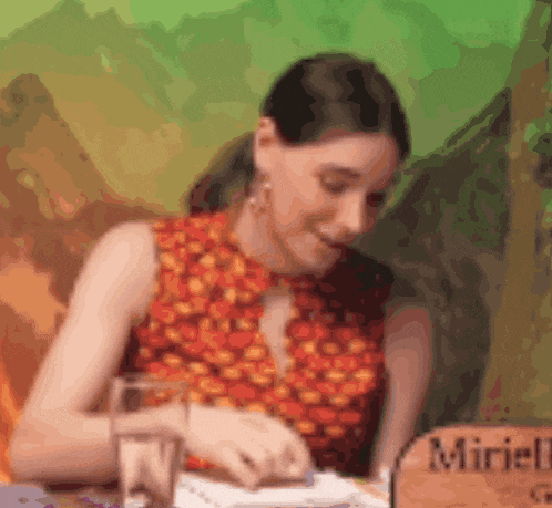 a woman sits at a table with a glass of water and a sign that says miniell