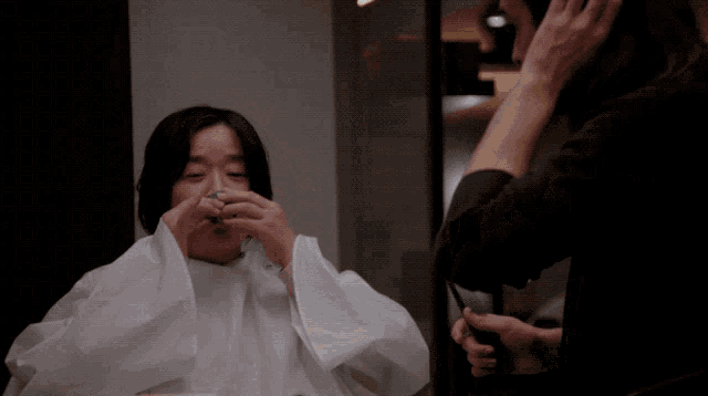 a woman is getting her hair cut by a man in a black jacket