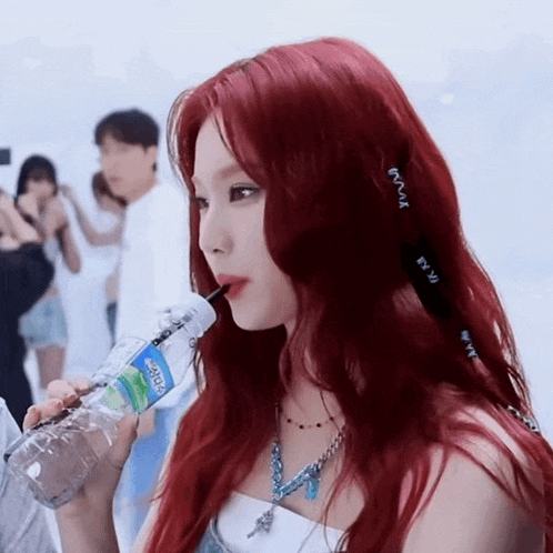 a woman with red hair is drinking water from a bottle with a straw