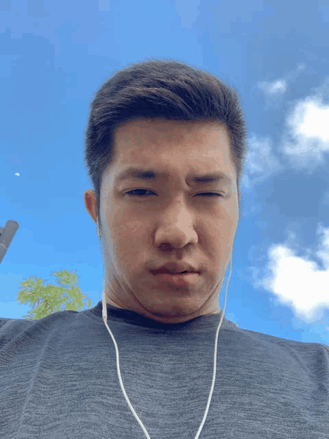 a man wearing ear buds looks at the camera with a blue sky in the background