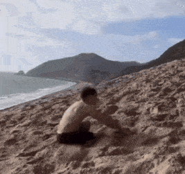 a man is sitting on top of a sandy hill near the ocean .