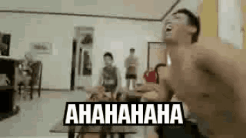 a man without a shirt is laughing in front of a group of people in a living room .