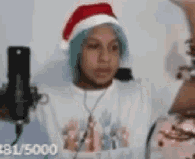 a person with blue hair is wearing a santa hat and a microphone .