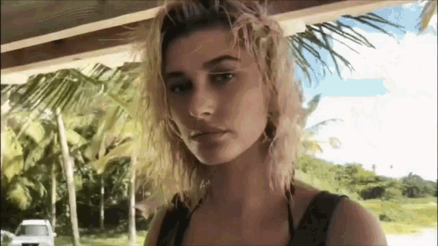 a woman in a bikini is standing in front of a palm tree and looking at the camera .