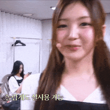 a girl with a microphone in her mouth looks at the camera while another girl looks at her phone