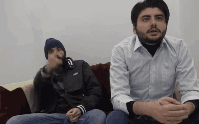 a man wearing a nike jacket sits next to another man on a couch